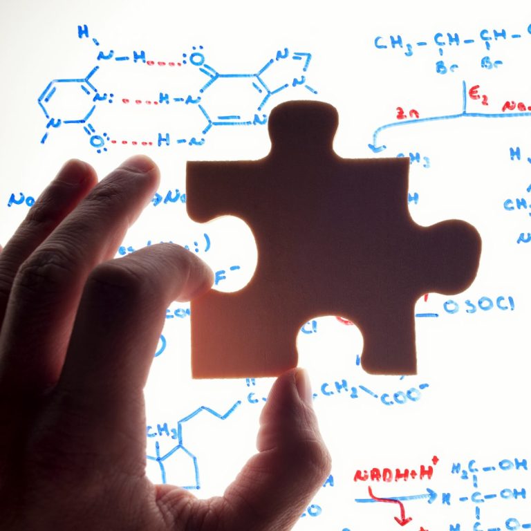 A hand holding a puzzle piece in front of a scientific diagram and molecular structures.